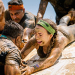 Participant smiling while holding the hand of her teammate to help him climb