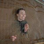 A woman smiling in water, beneath a cage