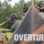Several people climb an obstacle with a rope