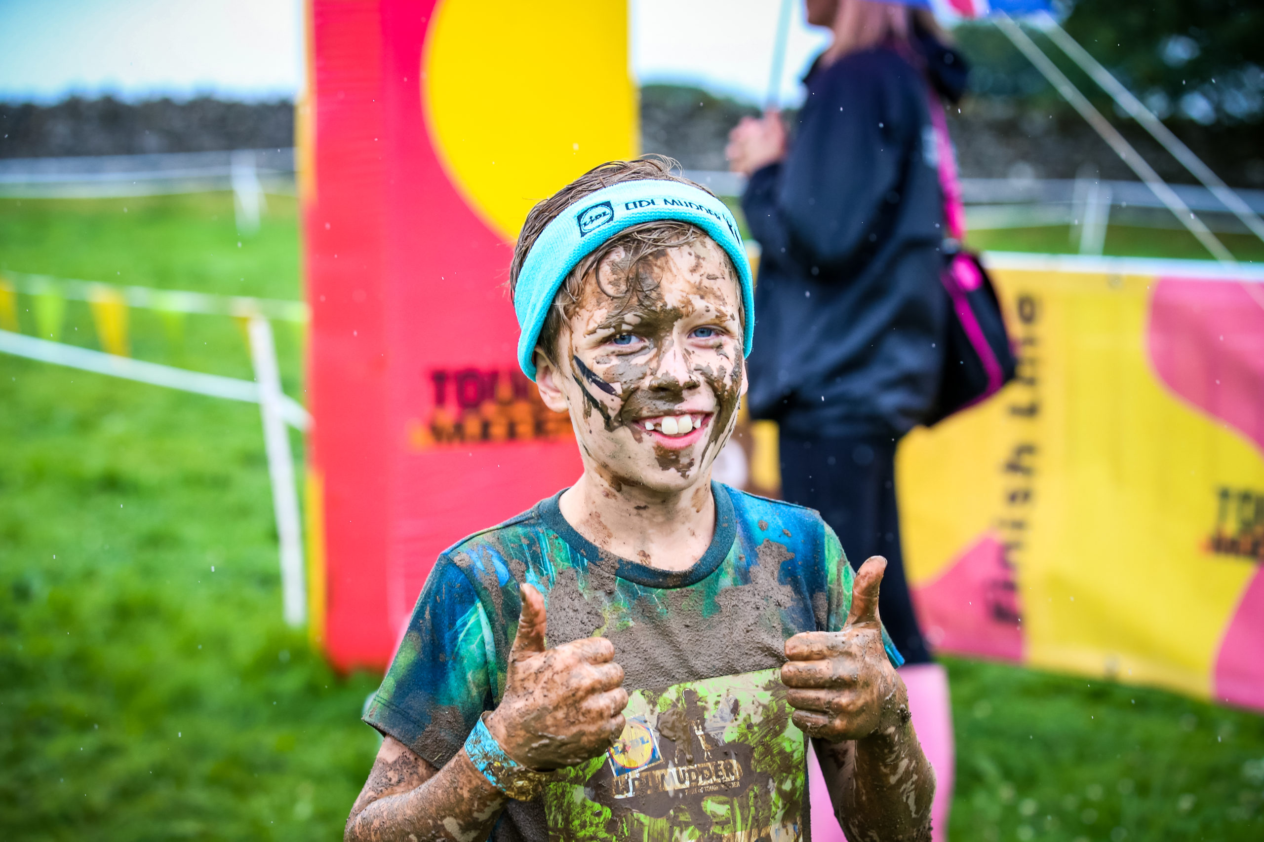 Muddy child in blue headband posing with 'thumbs up'