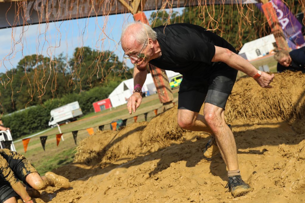 older man running mud obstacle