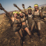 Participants covered with mud, smiling and waving at the camera